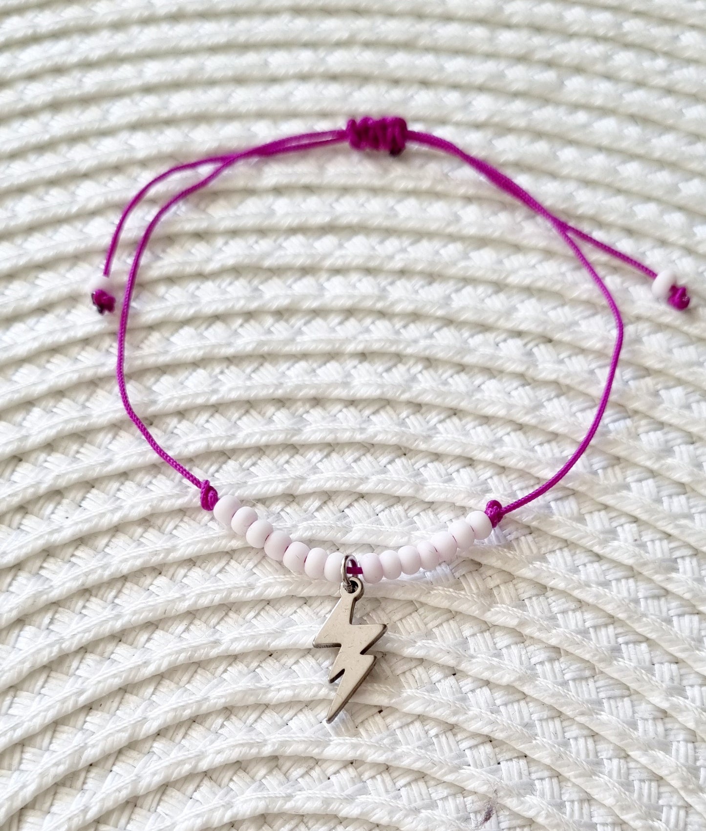 Pulsera realizada con hilo morado, con cierre de macramé y mini bolas de rocalla en tono blanco roto mate. Póntela en la muñeca izquierda para atraer energía positiva a tu vida.