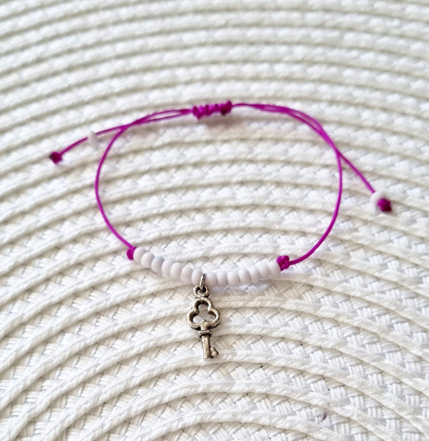 Pulsera realizada con hilo morado, con cierre de macramé y mini bolas de rocalla en tono blanco roto mate. Póntela en la muñeca izquierda para atraer energía positiva a tu vida.