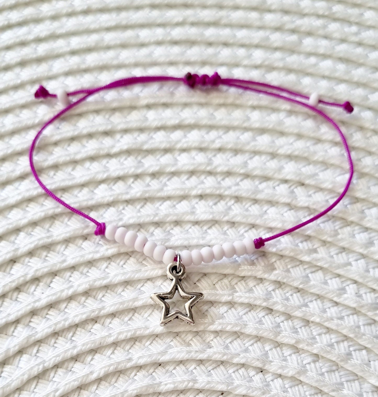 Pulsera realizada con hilo morado, con cierre de macramé y mini bolas de rocalla en tono blanco roto mate. Póntela en la muñeca izquierda para atraer energía positiva a tu vida.