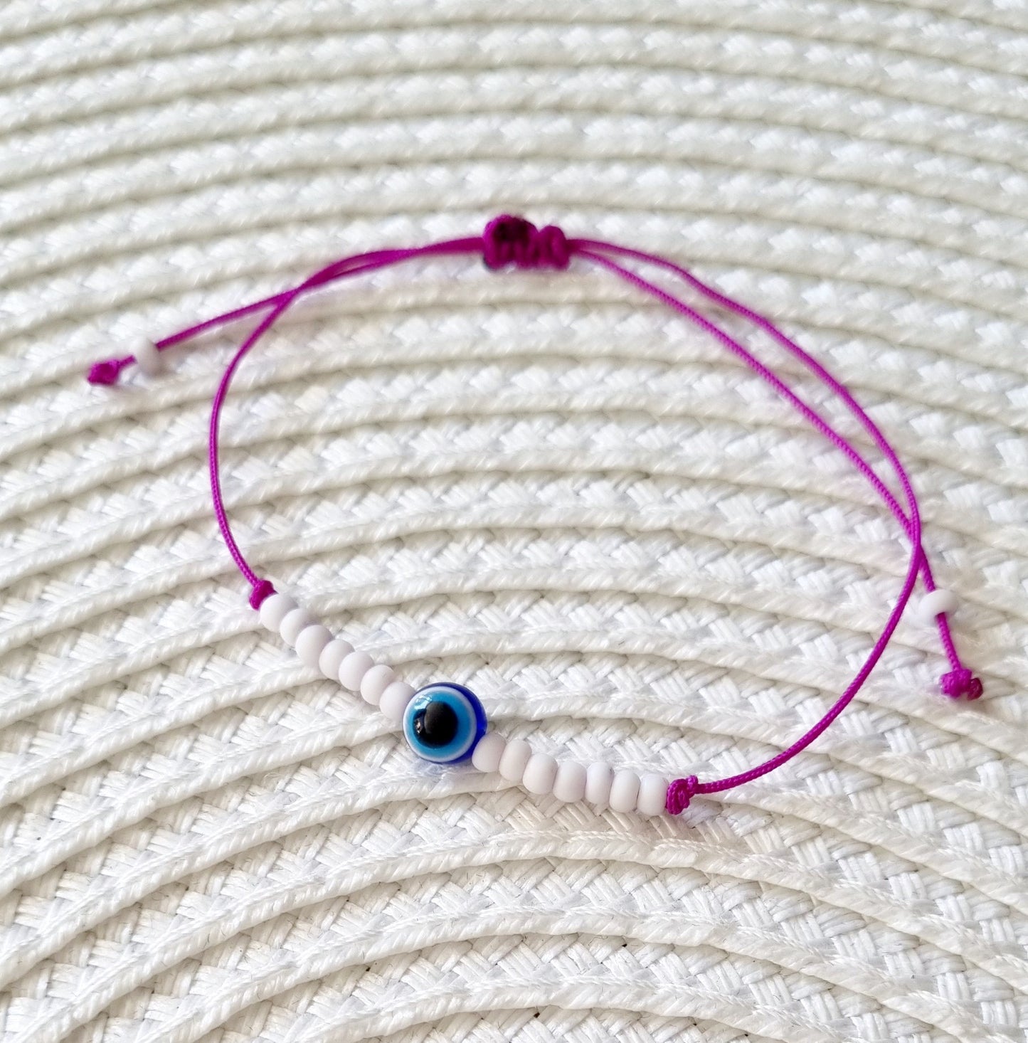 Pulsera realizada con hilo morado, con cierre de macramé y mini bolas de rocalla en tono blanco roto mate. Póntela en la muñeca izquierda para atraer energía positiva a tu vida.