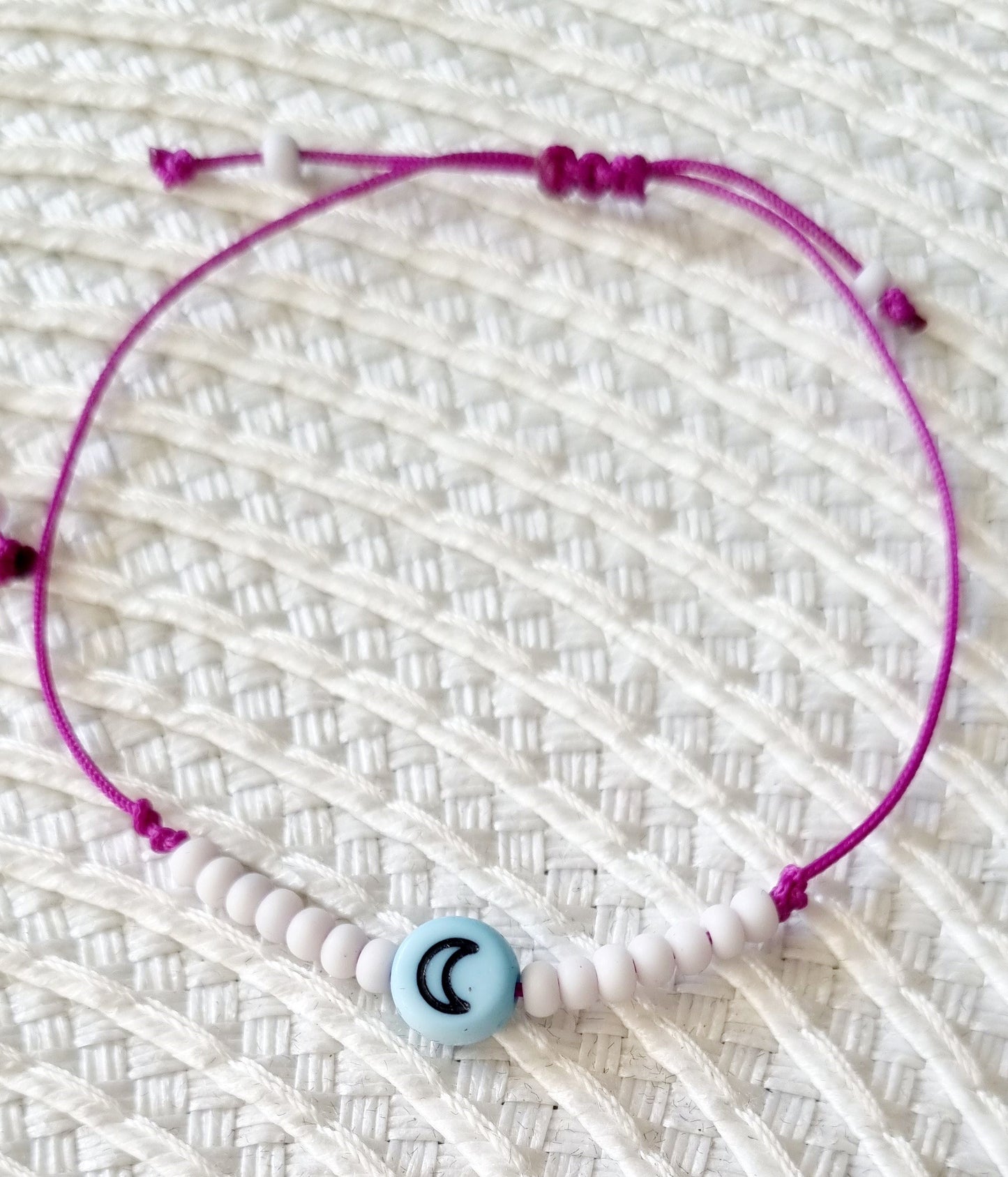 Pulsera realizada con hilo morado, con cierre de macramé y mini bolas de rocalla en tono blanco roto mate. Póntela en la muñeca izquierda para atraer energía positiva a tu vida.
