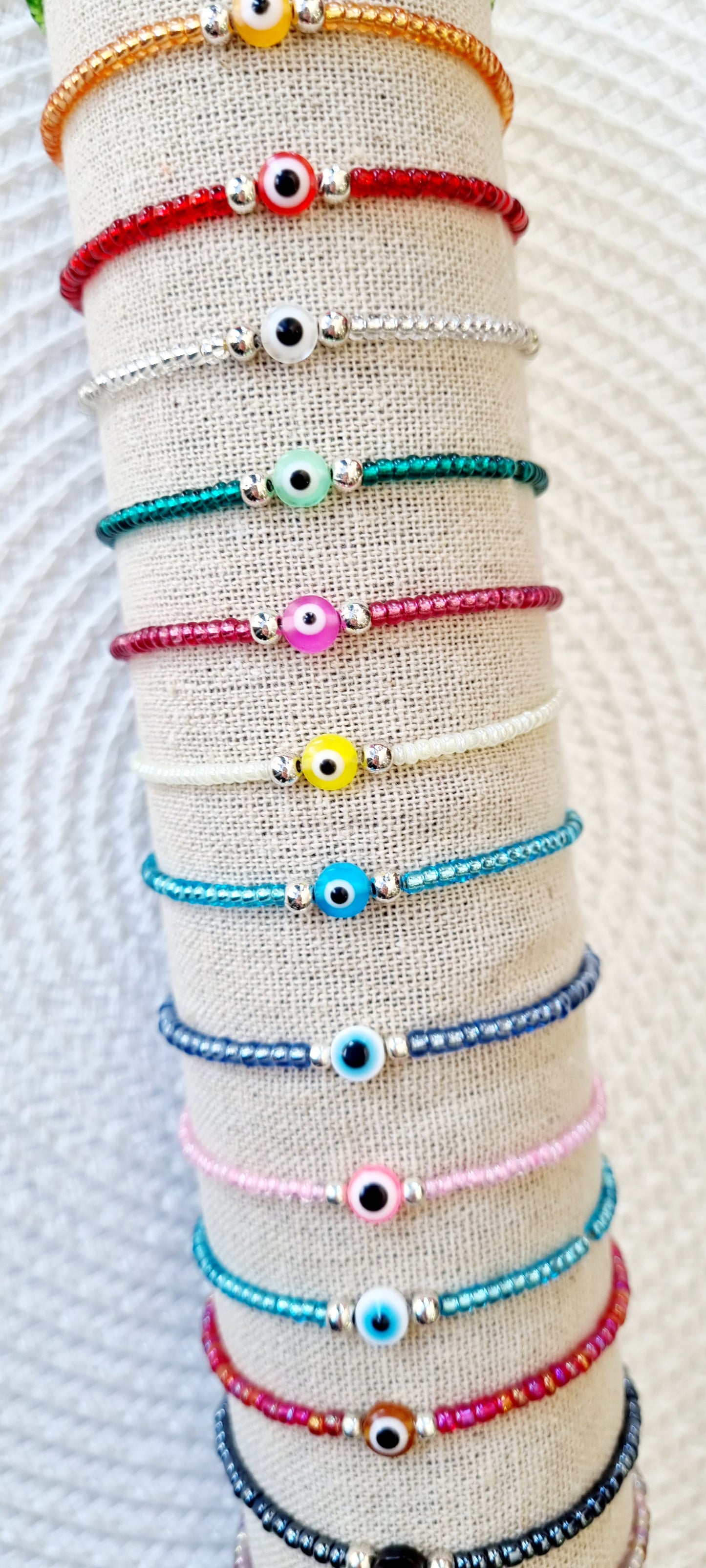 Pulsera elástica de protección ojo turco mini. Realizada con mini bolas de rocalla en tonos brillantes, entre piezas de acero y detalle de ojo turco en distintos colores.