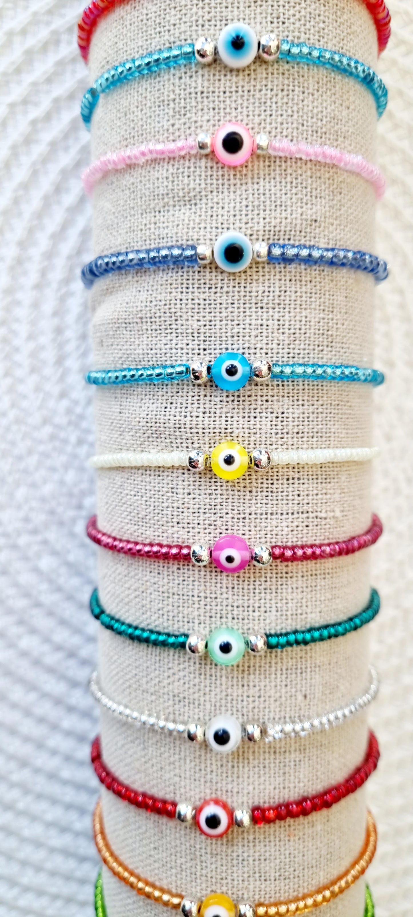Pulsera elástica de protección ojo turco mini.  Realizada con mini bolas de rocalla en tonos brillantes, entre piezas de acero y detalle de ojo turco en distintos colores.