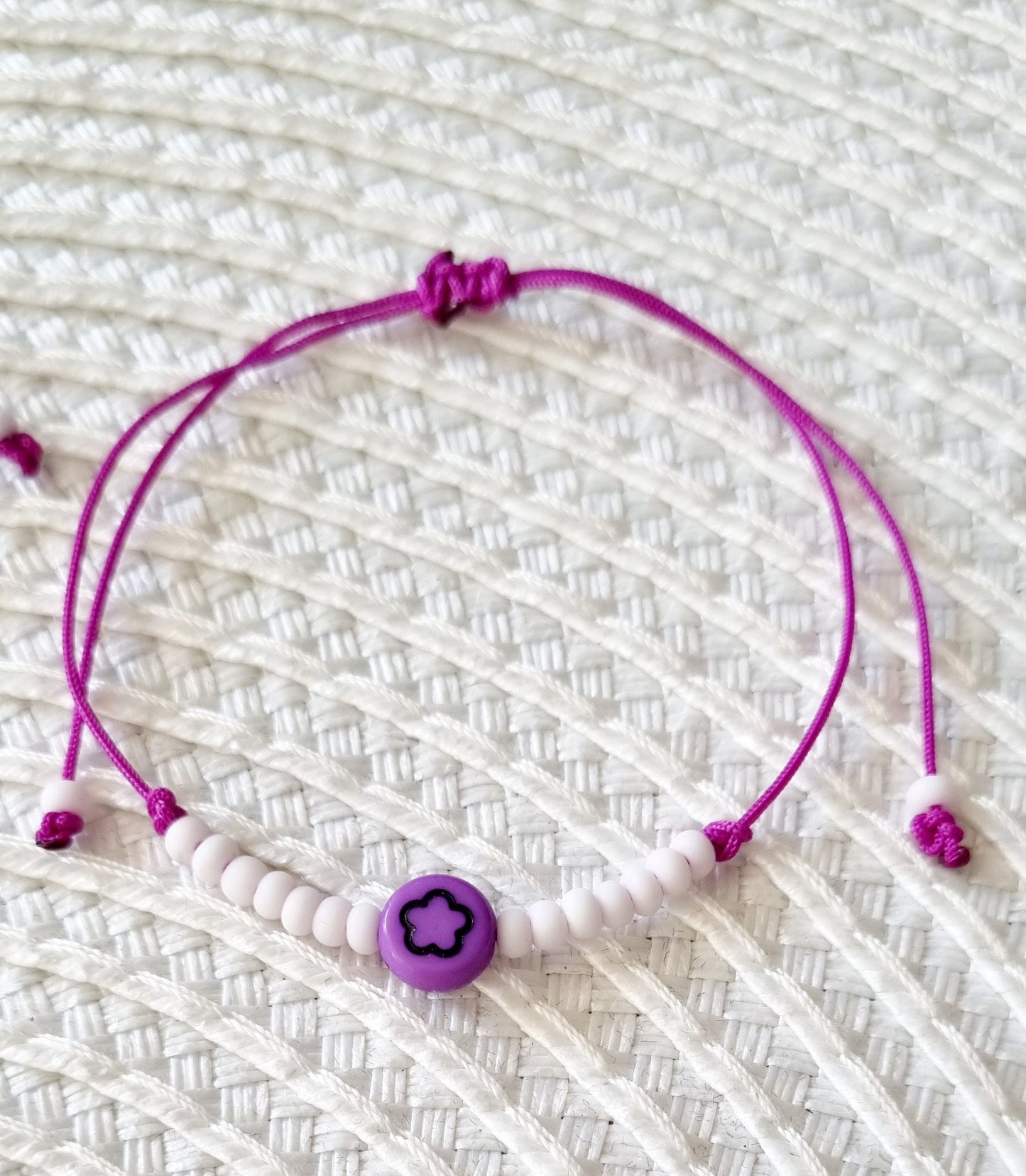 Pulsera realizada con hilo morado, con cierre de macramé y mini bolas de rocalla en tono blanco roto mate.   Póntela en la muñeca izquierda para atraer energía positiva a tu vida.