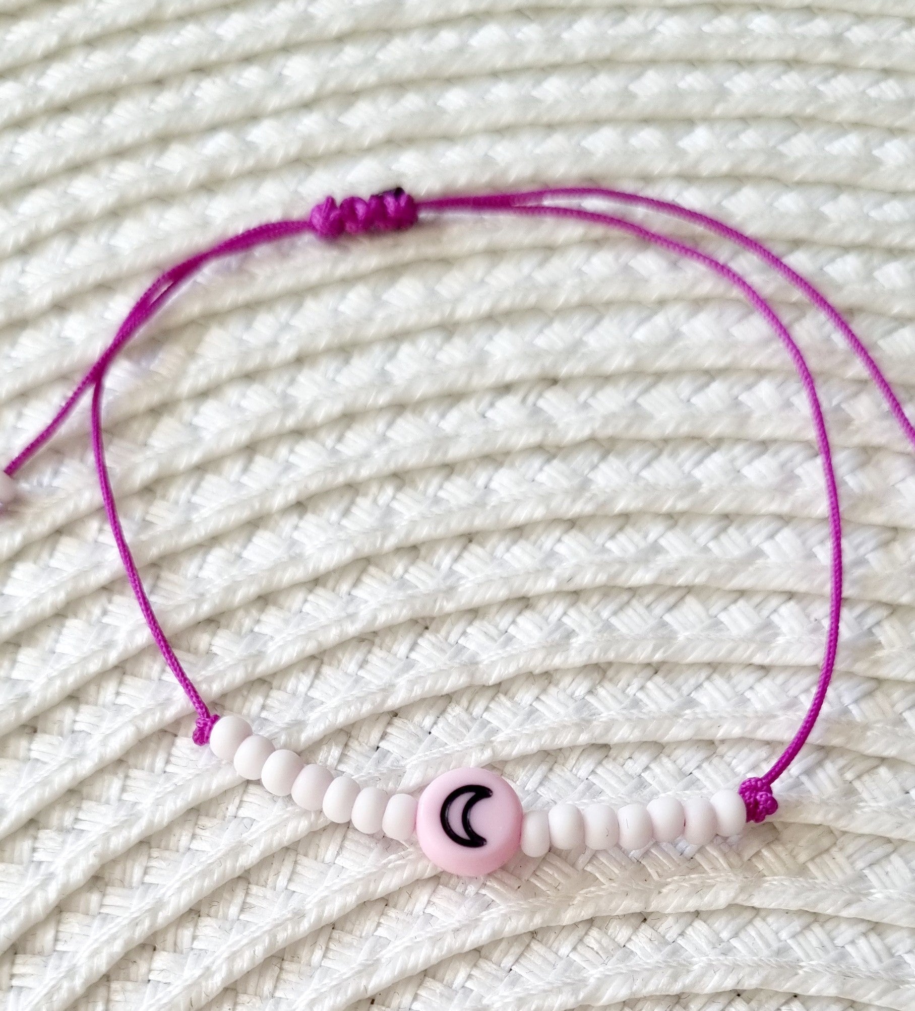 Pulsera realizada con hilo morado, con cierre de macramé y mini bolas de rocalla en tono blanco roto mate.   Póntela en la muñeca izquierda para atraer energía positiva a tu vida.