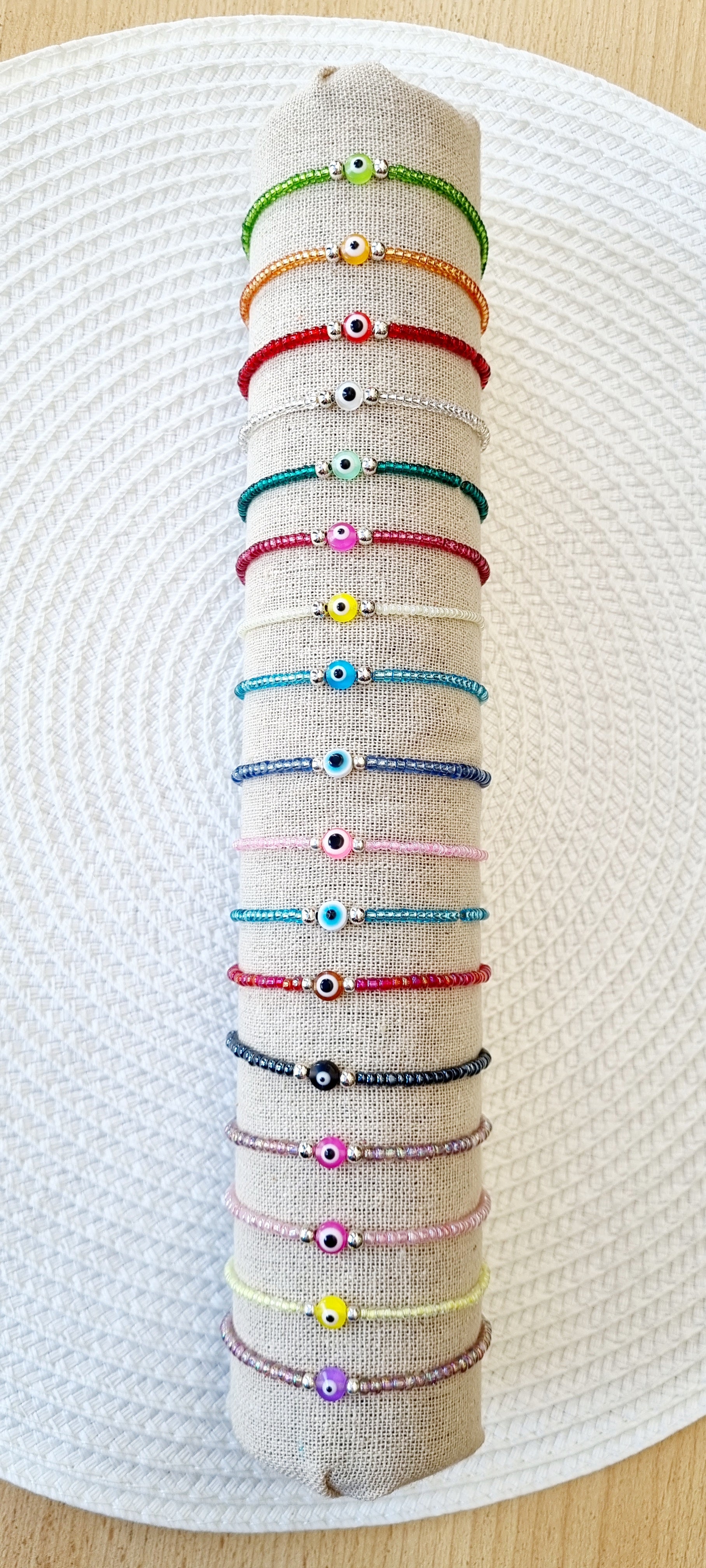 Pulsera elástica de protección ojo turco mini.  Realizada con mini bolas de rocalla en tonos brillantes, entre piezas de acero y detalle de ojo turco en distintos colores.