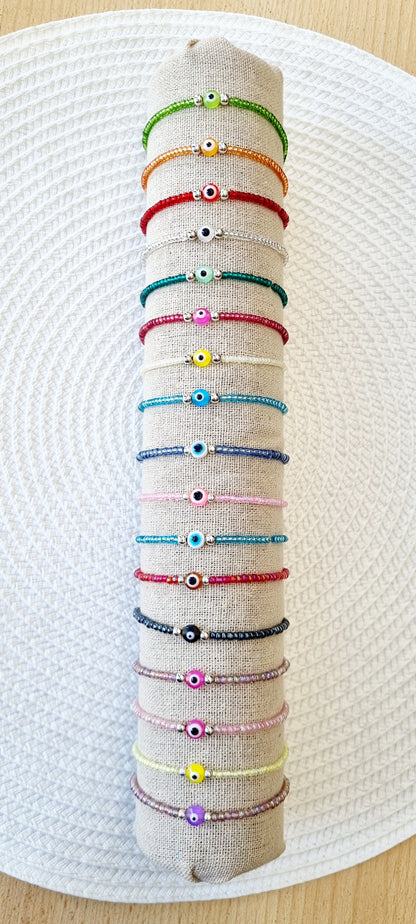 Pulsera elástica de protección ojo turco mini.  Realizada con mini bolas de rocalla en tonos brillantes, entre piezas de acero y detalle de ojo turco en distintos colores.