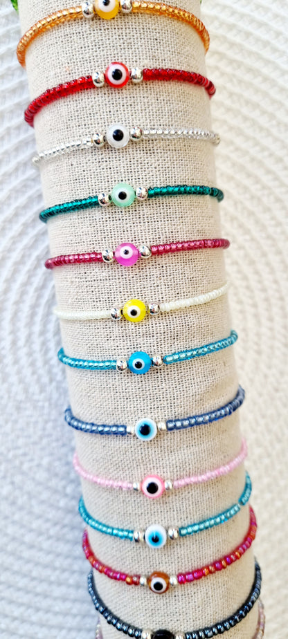 Pulsera elástica de protección ojo turco mini.  Realizada con mini bolas de rocalla en tonos brillantes, entre piezas de acero y detalle de ojo turco en distintos colores.