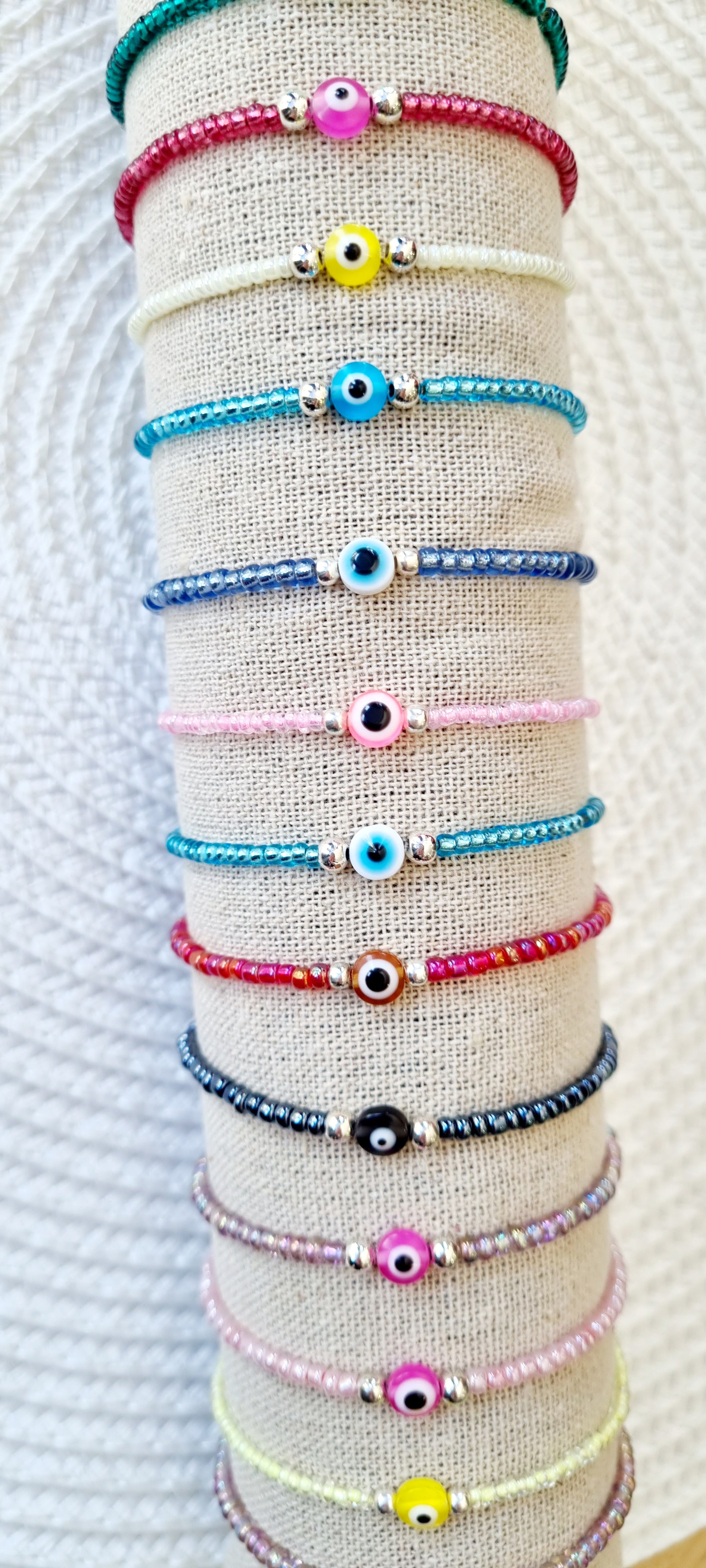 Pulsera elástica de protección ojo turco mini.  Realizada con mini bolas de rocalla en tonos brillantes, entre piezas de acero y detalle de ojo turco en distintos colores.