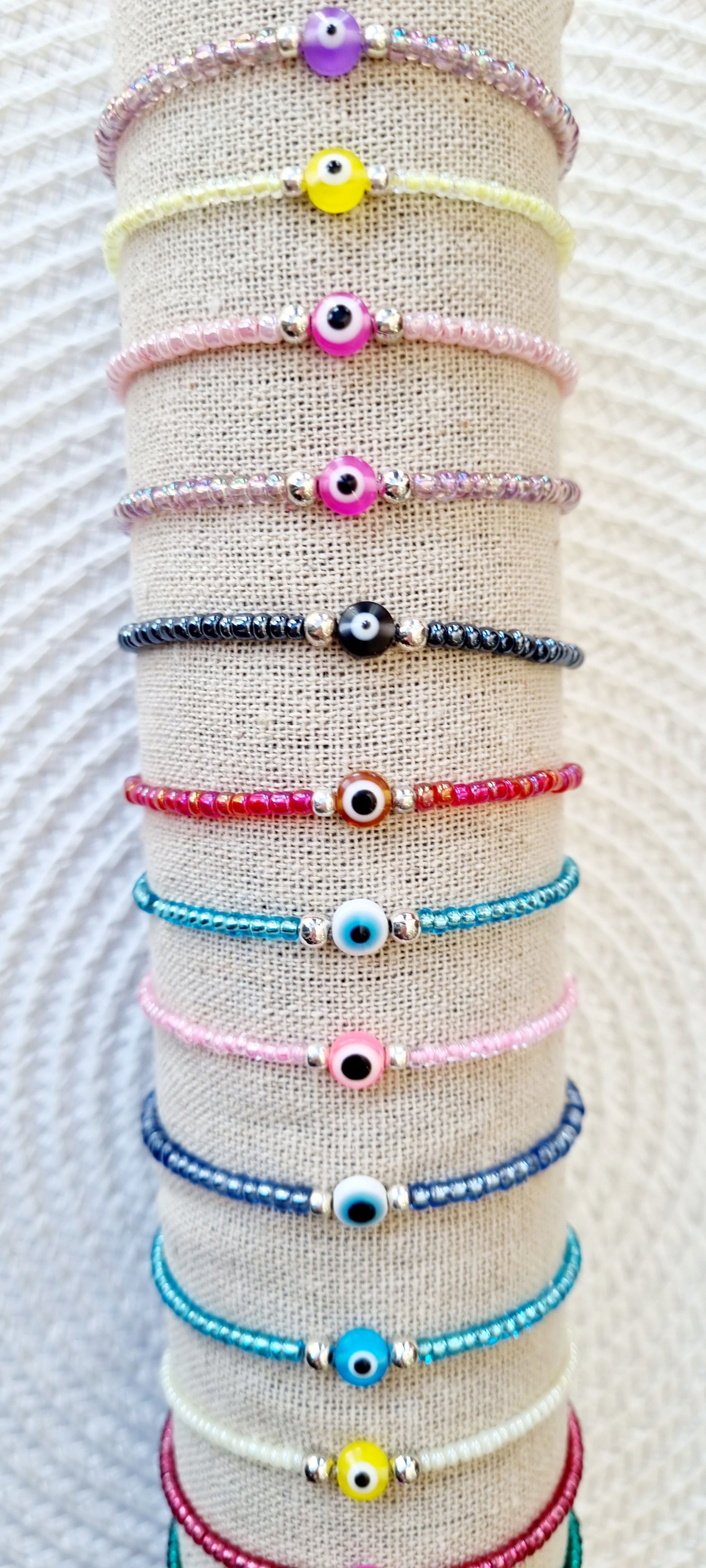 Pulsera elástica de protección ojo turco mini.  Realizada con mini bolas de rocalla en tonos brillantes, entre piezas de acero y detalle de ojo turco en distintos colores.