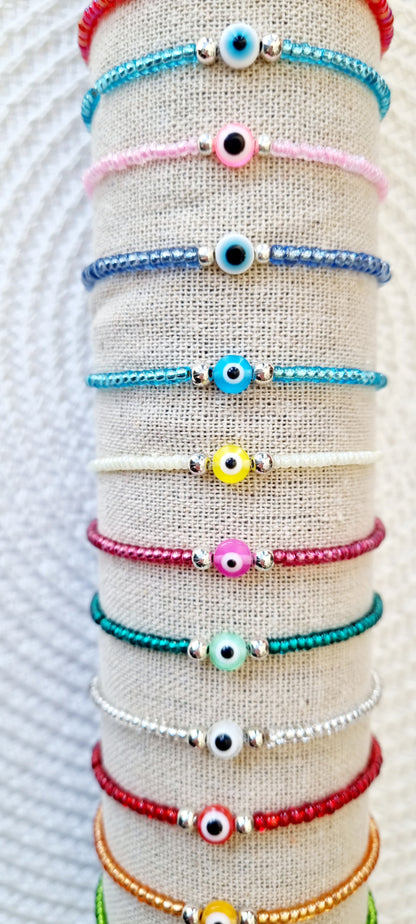 Pulsera elástica de protección ojo turco mini.  Realizada con mini bolas de rocalla en tonos brillantes, entre piezas de acero y detalle de ojo turco en distintos colores.